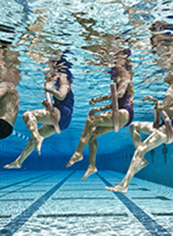 An image of people sitting on swimming noodles taken underwater. 